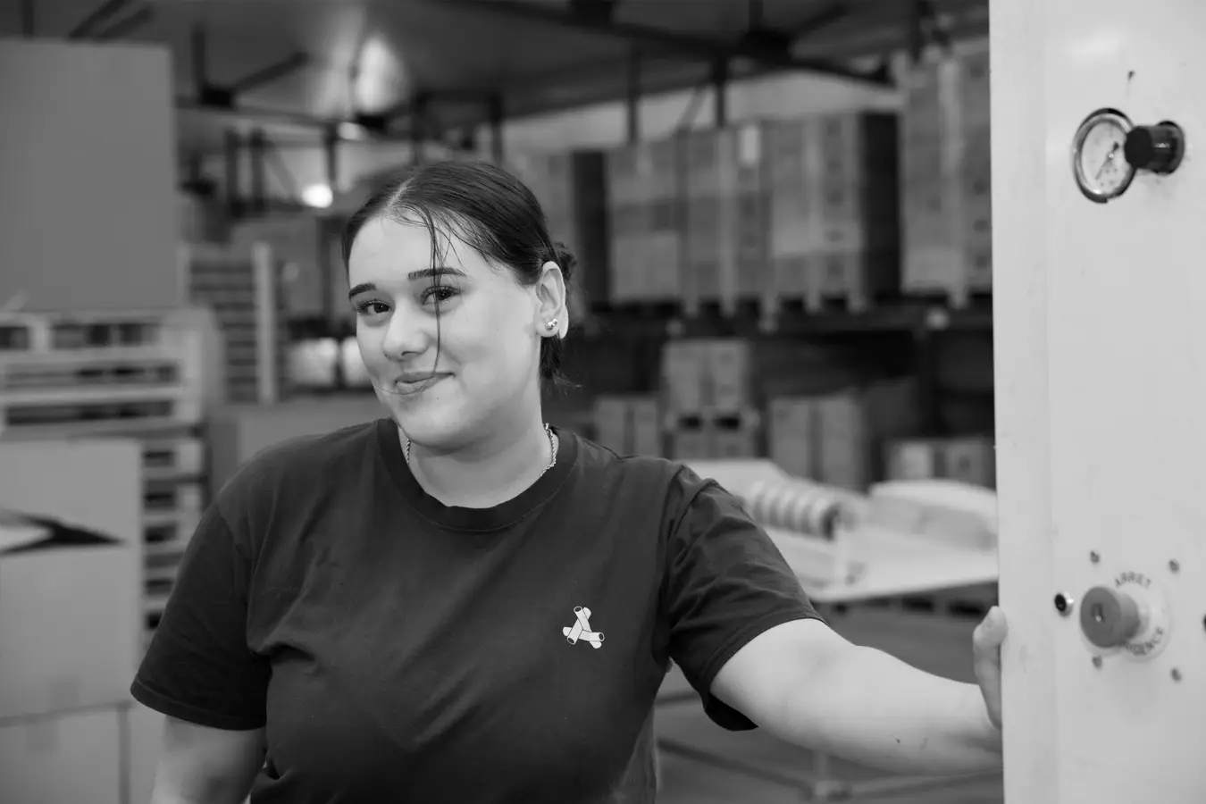 Collaboratrice souriante devant sa machine massicoteuse utilisée pour fabriquer des bagues en carton recyclé